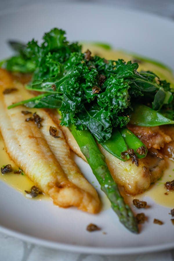 Close-up of a roasted fish fillet topped with asparagus and kale, drizzled with sauce.