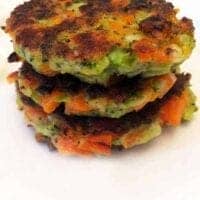 Three golden-brown vegetable patties are stacked on a white plate, with visible pieces of green and orange vegetables adding a colorful touch.