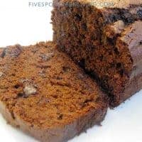 A close-up of a sliced chocolate chip zucchini bread loaf with a moist, rich texture and visible chocolate chips on a white background.