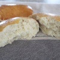 A close-up of homemade bread rolls, golden brown and broken in half on a patterned cloth, reveals their fluffy interior. The image includes the fivespot green living watermark in the corner.