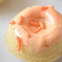 A mini round cake, reminiscent of Baked Pumpkin Doughnuts, is topped with light orange icing and orange sprinkles on a white surface. The image features the fivespot green LIVING watermark in the bottom right corner.