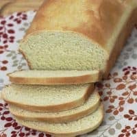 A loaf of homemade bread for sandwiches rests on a patterned cloth, with three slices fanned out in front. The bread has a golden crust and a soft, airy texture. The logo fivespot green living is in the lower right corner.