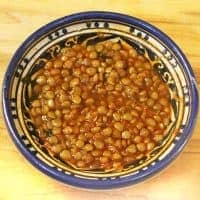 A blue and yellow decorative bowl filled with Moroccan lentils in a thick, brownish sauce, placed on a light wooden surface.