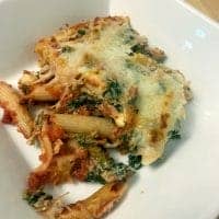A serving of baked penne pasta with tomato sauce, melted cheese, spinach, and herbs is presented in a white dish. This Healthy Vegetable Casserole Recipe features golden, slightly browned cheese on top.